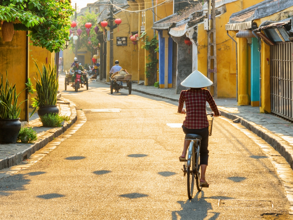 Vietnamese woman in traditional hat bicycling along Hoi An
